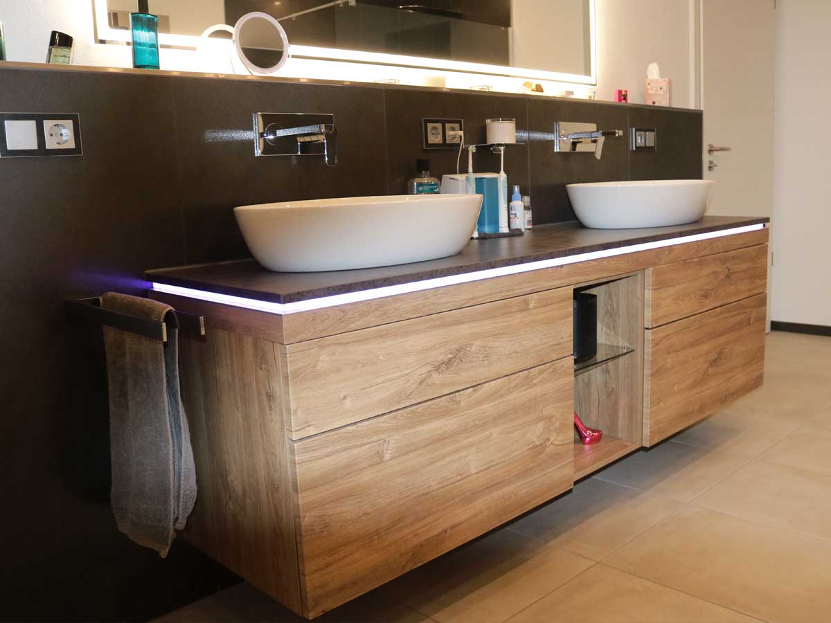 Modernes Badezimmer mit bodengleicher Dusche, großformatigen Wandfliesen in Natursteinoptik, schwarzer Glas-Duschabtrennung und dezent integrierter Nische für Pflegeprodukte.