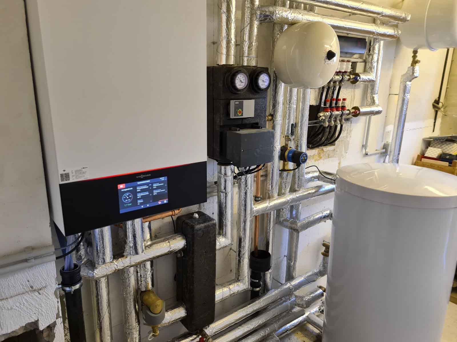 Heizungsanlage mit modernen, grauen Geräten der Marke Viessmann in einem sauber installierten Technikraum, inklusive Pufferspeicher, Rohrleitungen und Steuerungseinheit.